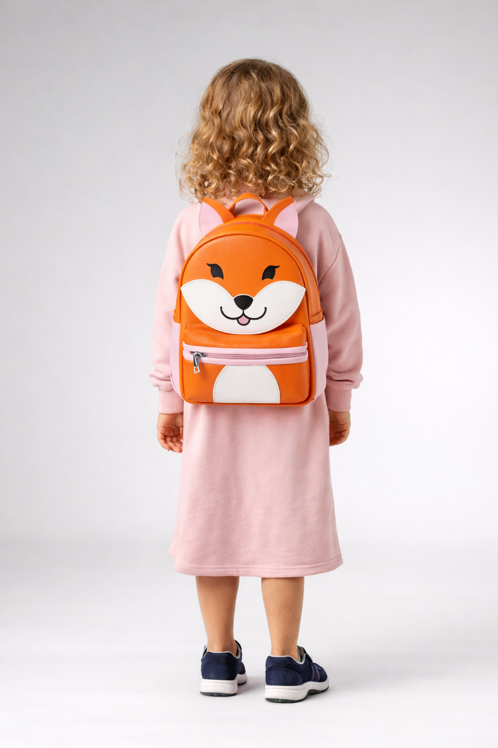 Child wearing a pink dress and fox-themed backpack on a white background