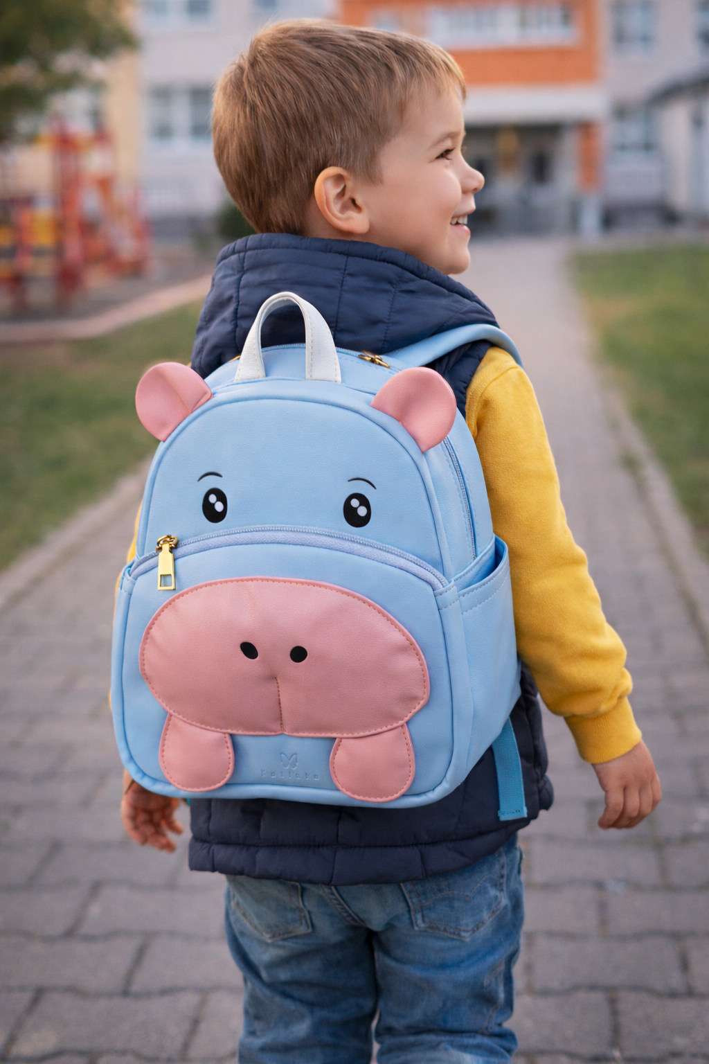 Child wearing a blue hippo-shaped backpack on a sidewalk.